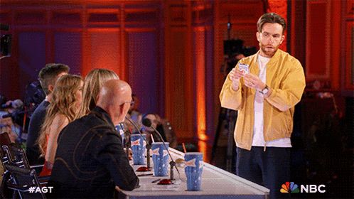 a man in a yellow jacket holds a card in front of a nbc logo