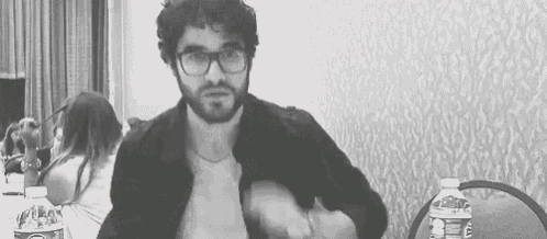 a man with a beard and glasses is sitting at a table with a water bottle .