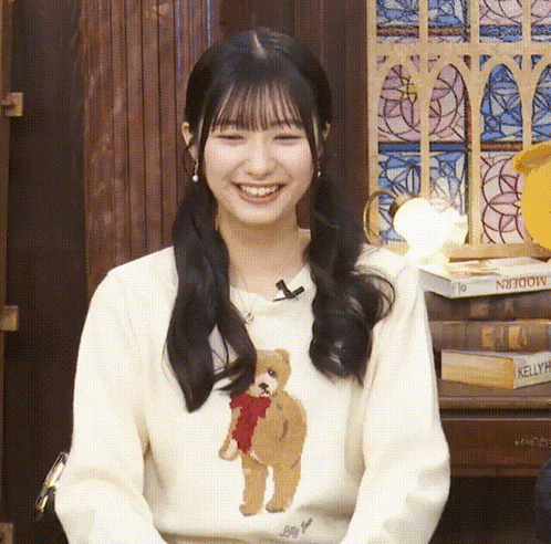 a woman wearing a sweater with a teddy bear on it is smiling
