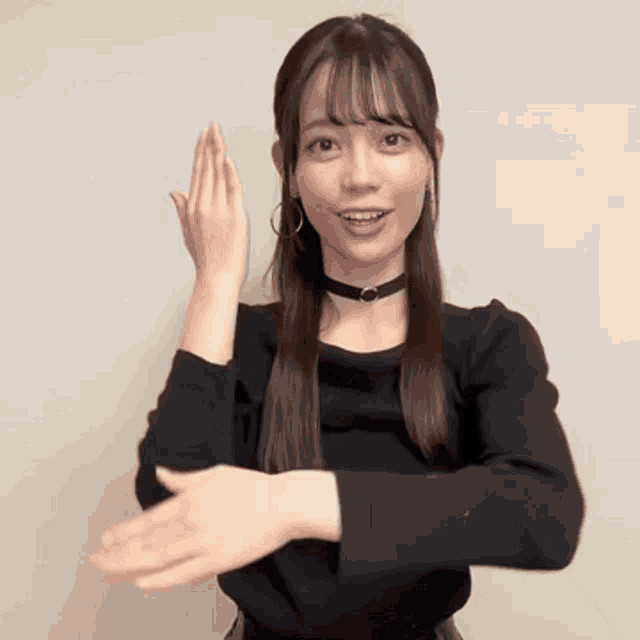 a woman wearing a choker and a black sweater is making a gesture with her hands