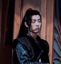 a young man with long black hair is standing in front of a wooden wall .