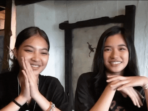 two girls are sitting next to each other with their hands on their faces and one has a monkey on the wall behind them