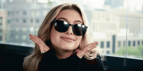 a woman wearing sunglasses and a black shirt is making a peace sign with her hands .