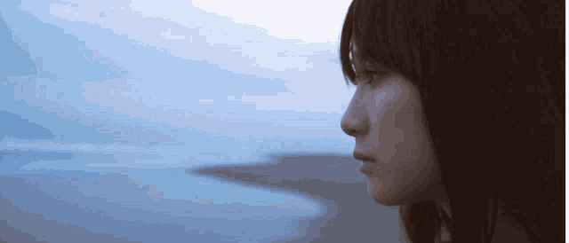 a close up of a woman 's face with the ocean in the background