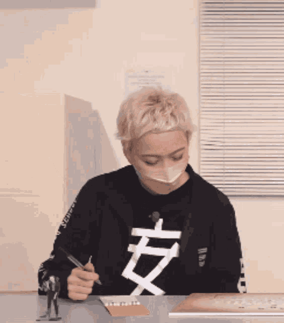 a person wearing a black shirt with chinese characters on it is writing on a piece of paper