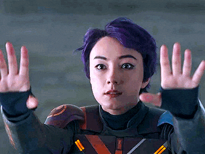 a woman with purple hair is making a funny face with her hands outstretched .
