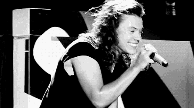 harry styles is smiling while singing into a microphone .