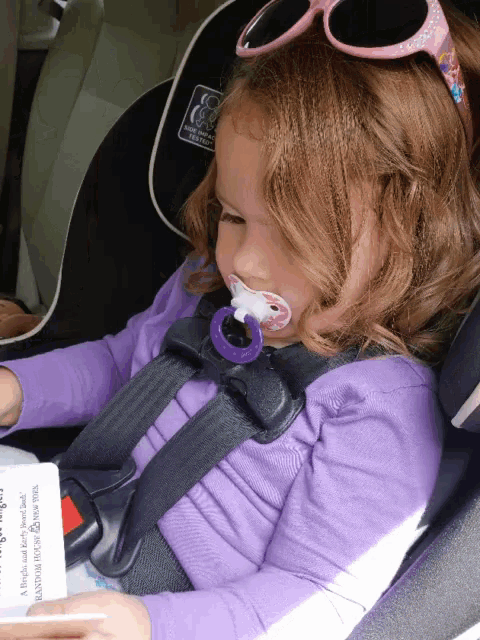 a little girl wearing sunglasses and a pacifier in her mouth is sitting in a car seat