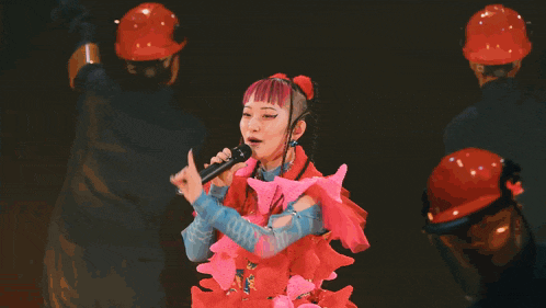 a woman with pink hair singing into a microphone while wearing a colorful outfit