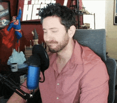 a man in a pink shirt is sitting in front of a microphone in front of a sign that says " i am he "