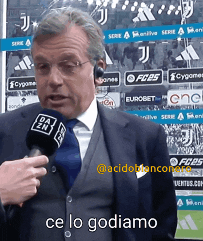 a man in a suit and tie is talking into a microphone with the words ce lo godiamo in the corner