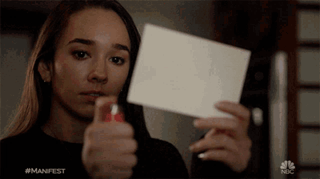 a woman holding a piece of paper with the nbc logo on the bottom