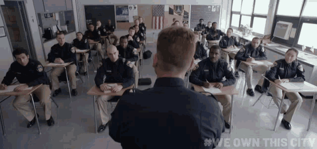 a group of police officers are sitting at desks in a classroom with #we own this city written on the bottom
