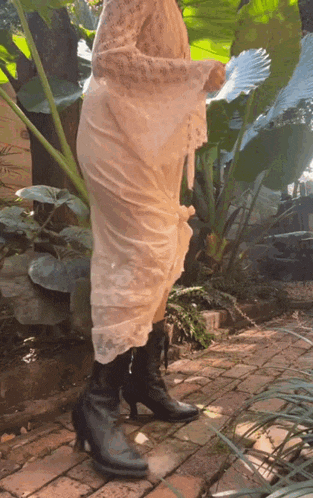 a woman in a white dress and black boots is standing on a brick sidewalk