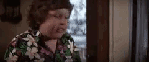a woman in a floral shirt is standing in front of a door and looking out the window .