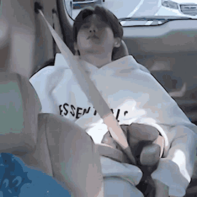 a person wearing a white essentials sweatshirt is sleeping in a car