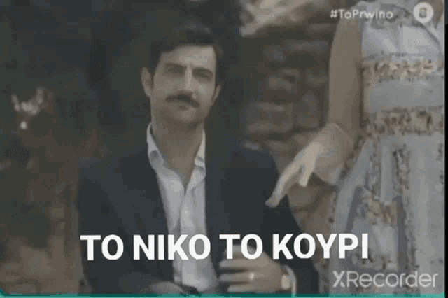 a man in a suit is pointing at a woman in a dress and the words to niko to koypi are above him .