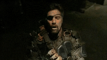 a close up of a person wearing a helmet and holding a gun in a dark room .