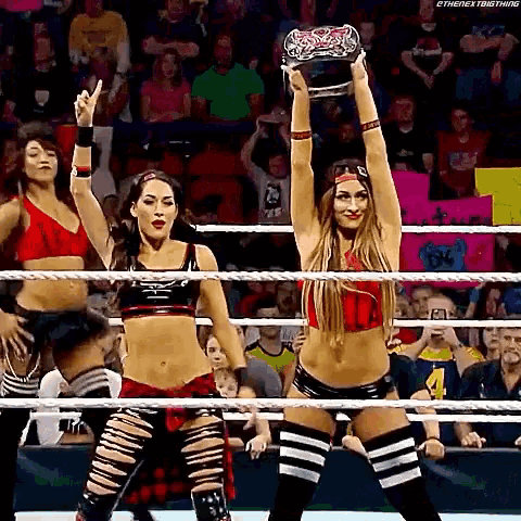 a couple of women are standing in a wrestling ring holding a championship .