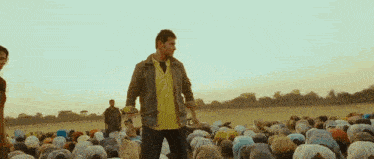 a man in a yellow shirt is standing in front of a crowd of people praying .