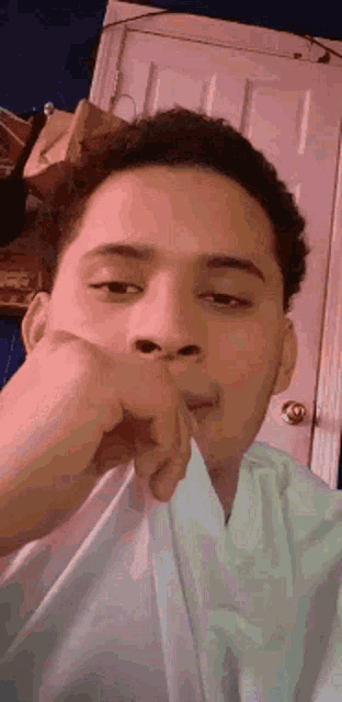 a young man covering his mouth with his hand in front of a door .