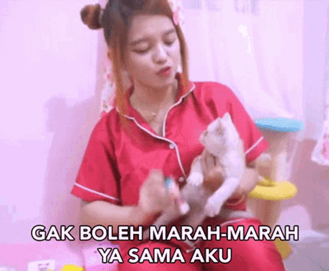 a woman in a red shirt is holding a kitten and says " gak boleh marah-marah ya sama aku " .
