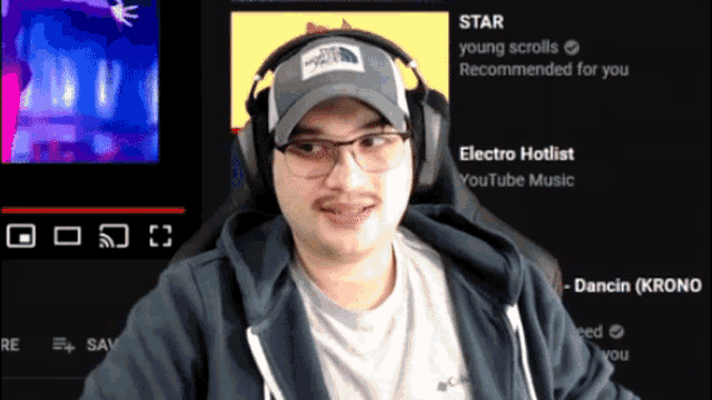 a man wearing headphones and a hat is sitting in front of a screen that says electro hotlist