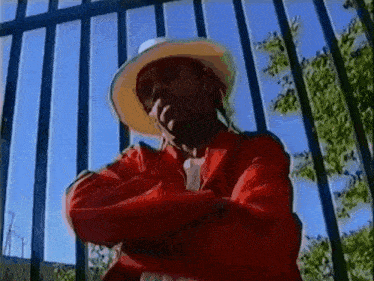 a man wearing a red jacket and a white hat is standing in front of a fence .
