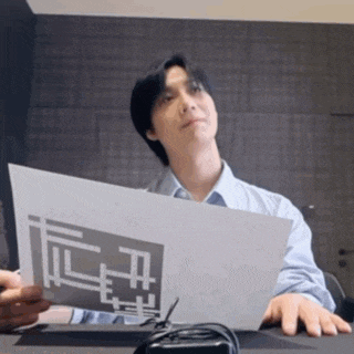 a man is sitting at a desk holding a piece of paper with a geometric design on it