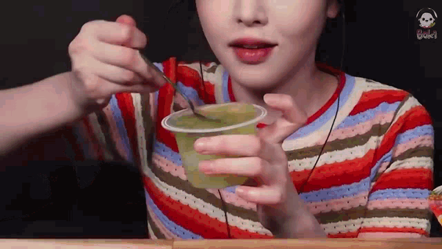 a woman in a colorful striped shirt is eating a green smoothie with a spoon .