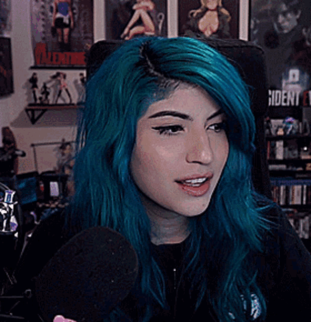 a woman with blue hair is talking into a microphone in front of a shelf that says resident evil