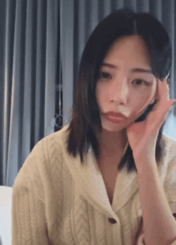 a woman wearing a white sweater is making a face with her hand