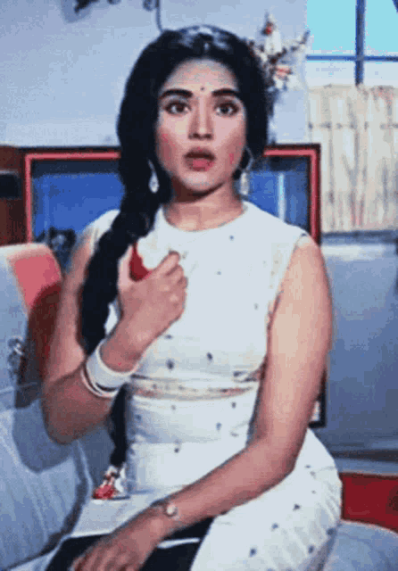 a woman in a white dress is sitting on a couch with her hand on her chest