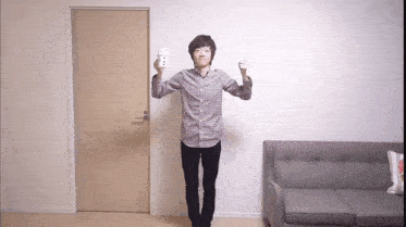 a man in a plaid shirt is standing in front of a door holding a remote control