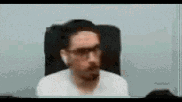 a blurry image of a man wearing glasses and a white shirt