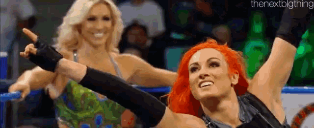 a couple of women are standing next to each other in a wrestling ring and one of them is pointing at the camera .
