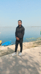 a man standing in front of a body of water with a boat in the background