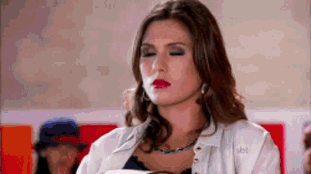 a woman with her eyes closed is wearing a white jacket and necklace .