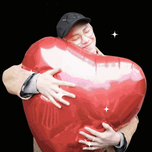 a man is hugging a heart shaped balloon with the letter p on his hat