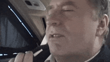 a man is sitting in a car with his eyes closed and his mouth open