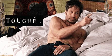 a shirtless man is laying on a bed and pointing at the camera with the word touche written above him