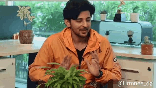 a man wearing an orange jacket is sitting in front of a plant