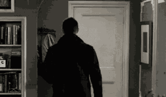 a man in a black coat is walking through a doorway in a hallway .