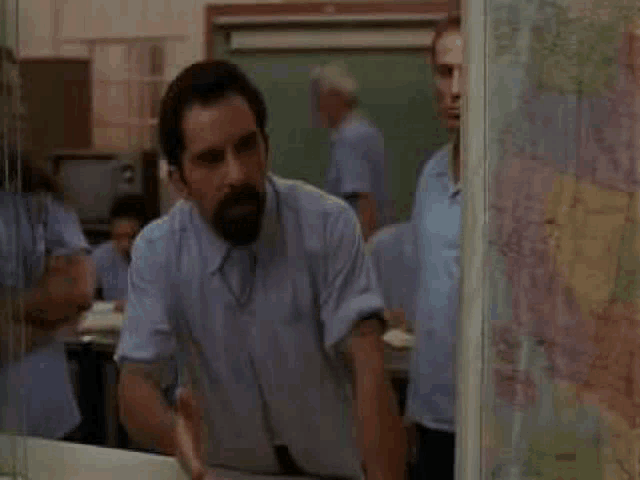a man with a beard is standing in front of a large map in a room .