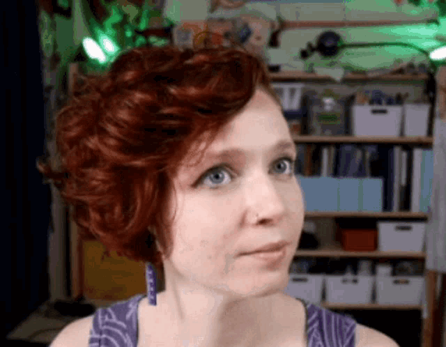 a woman with red hair is wearing a purple shirt and earrings