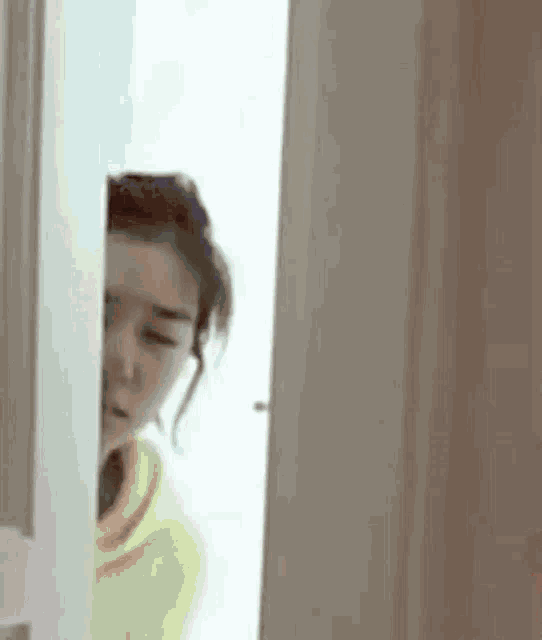 a woman in a yellow hoodie is peeking out of a door .