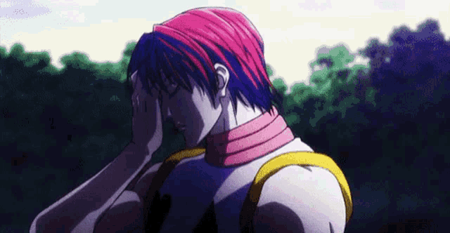 a man with pink hair is holding his head while standing in a forest .