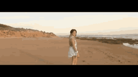 a woman in a white dress is walking along a sandy beach .