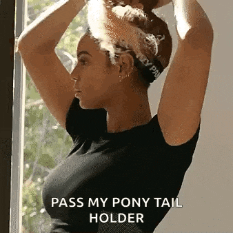 a woman in a black shirt is holding her hair in a ponytail holder .