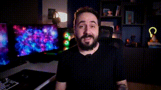 a man with a beard is sitting in front of a computer monitor and making a face .